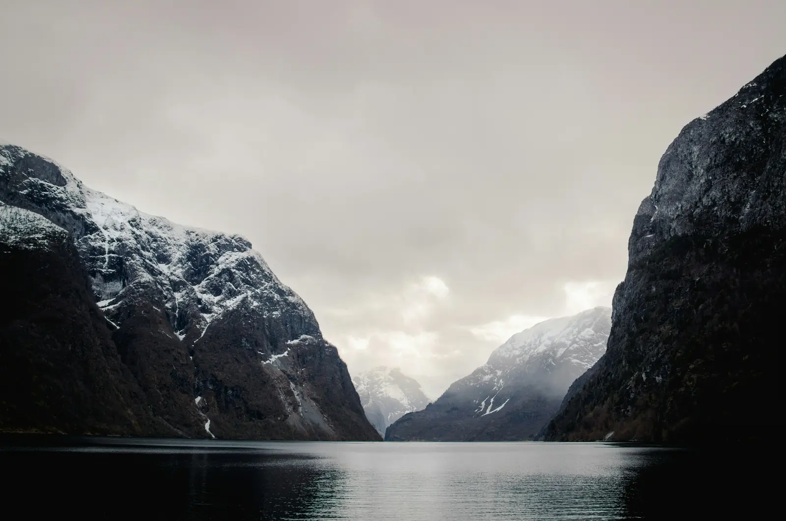 Nærøyfjordens mörka vatten mellan höga fjäll i låga moln