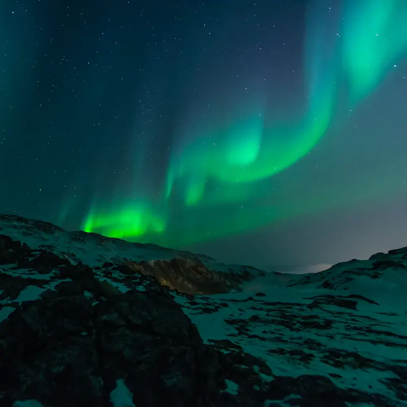 Grönt norrsken över ett snötäckt landskap vid Tromsø